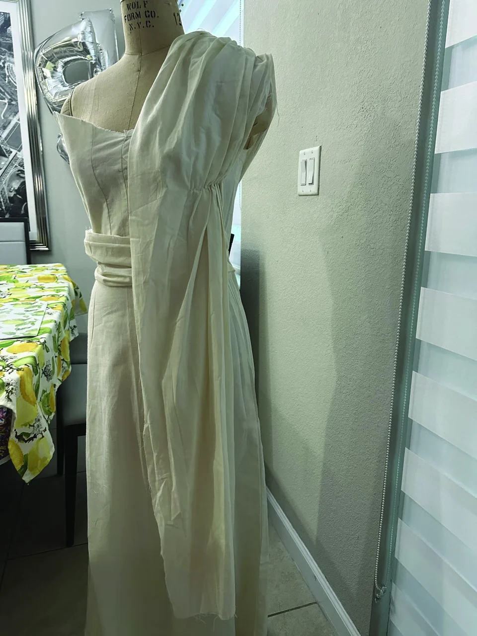 White draped Faith garment in progress on a dress form, side view.